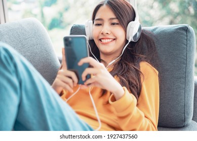 Happy asian woman using mobile smartphone and headphones while listening online music media entertainment relaxation in a sofa at home. - Shutterstock ID 1927437560