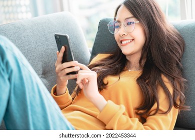 Happy asian woman using mobile phone. Smiling young female using app shopping online, ordering delivery relax on sofa at home. - Shutterstock ID 2022453344