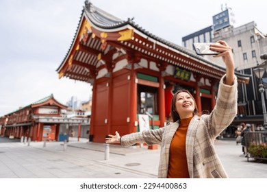 Happy Asian woman using mobile phone taking selfie during travel Sensoji Temple at Asakusa district, Tokyo, Japan. Attractive girl enjoy urban outdoor lifestyle travel city street on holiday vacation.