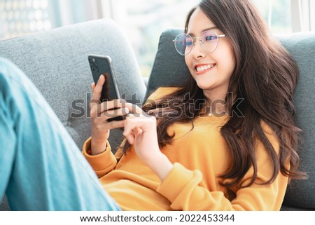 Happy asian woman using mobile phone. Smiling young female using app shopping online, ordering delivery relax on sofa at home.