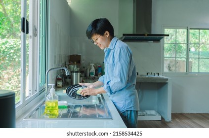 Happy Asian woman washing dishes with dirty food scraps Cleaner in the sink on the kitchen counter.