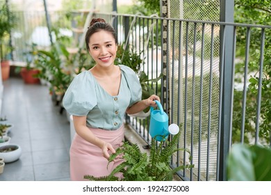 Happy Asian Woman Watering Plant On The Balcony.