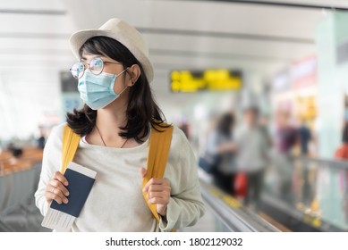 Happy Asian Woman Wear Protective Face Mask And Eyeglasses Walking In International Airport Terminal During Virus Pandemic. Smiling Young Female Traveler With Yellow Backpack At The Departure Hall