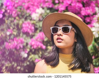 Happy Asian woman wearing hat and sunglassses with pink bokeh background in sunny day.