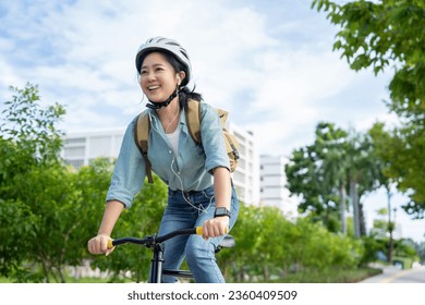 Happy Asian woman wearing a helmet and listening to her favorite music while riding a bicycle through a city park. - Powered by Shutterstock