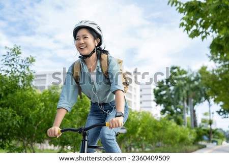 Happy Asian woman wearing a helmet and listening to her favorite music while riding a bicycle through a city park.
