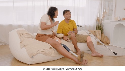 Happy Asian woman wearing prosthetics leg and couple man with leg disabilities watching television enjoys moment cheering excitement football soccer match sports game together on their sofa at home - Powered by Shutterstock