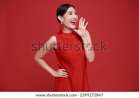 Happy Asian woman wearing red dress with open mouths raising hands shouting announcement isolated on red copy space background. 