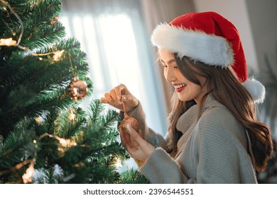 Happy asian woman wearing a Santa hat and holding Christmas ornament for decorate on Christmas tree preparing for season greeting of merry Christmas and happy new year holiday. - Shutterstock ID 2396544551