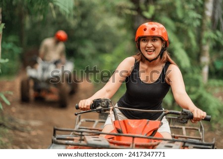 happy asian woman wearing savety helmet while riding atv through the track at amusement park spending her holiday