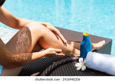 Happy Asian Woman Wearing Swimsuit, Hat Lying On Sunbed Applying Sun Cream And Relaxing At The Poolside. Sunburn Protection. Summer Holidays And Vacation Concept.