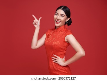 Happy Asian woman wearing traditional cheongsam qipao dress hand pointing up to copy space isolated on red background. Happy Chinese new year - Shutterstock ID 2080371127