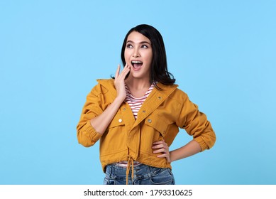 Happy asian woman in yellow shirt and mouth open over blue background.