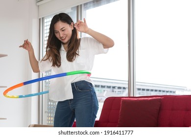 Happy Asian women playing Hula Hoop in the living room at home. Young adult woman learning to play with a hula-hoop in a living room.