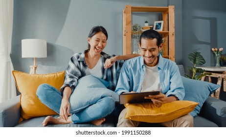 Happy Asian Young Attractive Couple Man And Woman Sit On Couch Use Tablet Shopping Online Furniture Decorate Home In The Living Room At New House. Young Married Moving Home Shopper Online Concept.