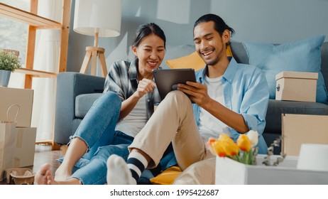 Happy asiatische junge attraktive Paar Mann und Frau nutzen Tablet-Online-Shopping Möbel schmücken Haus mit Karton-Paket Umzug in neues Haus. Junge verheiratete asiatische Heimkäufer Online-Konzept.