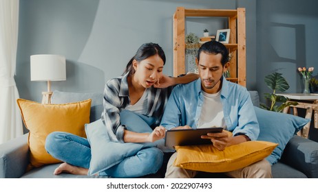 Happy Asian Young Attractive Couple Man And Woman Sit On Couch Use Tablet Shopping Online Furniture Decorate Home In The Living Room At New House. Young Married Moving Home Shopper Online Concept.