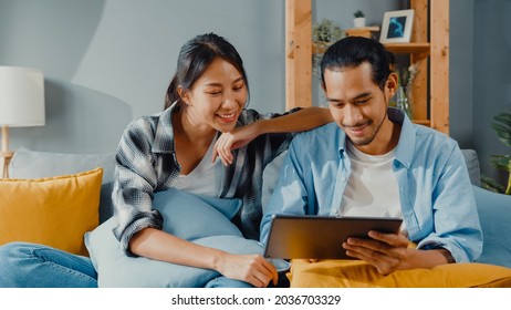 Happy Asian Young Attractive Couple Man And Woman Sit On Couch Use Tablet Shopping Online Furniture Decorate Home In The Living Room At New House. Young Married Moving Home Shopper Online Concept.