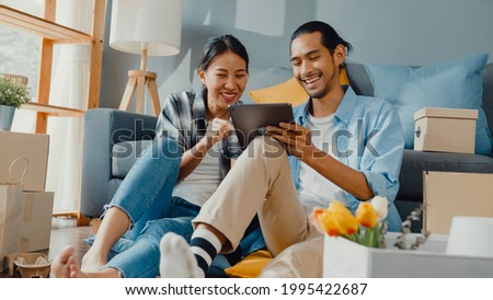 Happy asian young attractive couple man and woman use tablet online shopping furniture decorate house with carton package move in new house. Young married asian moving home shopper online concept. 商業照片 © 