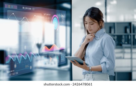 Happy asian young businesswoman using digital tablet with business finance chart dashboard on virtual screen and standing in office  working space, Business finance data analytics and market concept. - Powered by Shutterstock