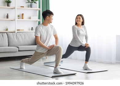 Happy asian young couple exercising together at home, positive korean man and woman in sportswear standing on fitness mat, stratching and having conversation, copy space. Healthy lifestyle concept