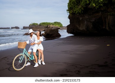 happy asian young couple riding bicycles on black sandy beach - Powered by Shutterstock