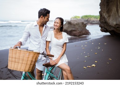 happy asian young couple riding bicycles on black sandy beach - Powered by Shutterstock