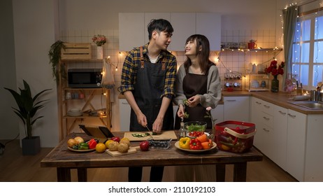 Happy Asian Young Couple Working Together Making Valentine’s Day Dinner In A Cozy Decorated Kitchen At Home