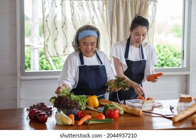 Happy Asian Young Daughter And Senior Mother Cooking Online  Class On Tablet Together Making Fresh Vegetables Food In Kitchen At Home