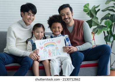 Happy Asian young LGBTQ gay couple and little cute adopted Caucasian   African kid smiling   showing rainbow family drawing in living room at home  LGBT diverse family concept
