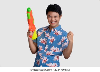 Happy Asian young man holding a water gun isolated on white background. He shows signs, yes.