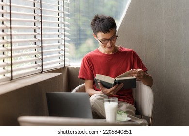 Happy Asian Young Man Reading A Book In Cafe.