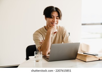 Happy Asian Young Man Studying With Book And Laptop Computer In Bright Room At Home