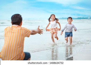 Happy Asian Young Single Dad Playing With His Children Boy And Girl, They Running On Sandy Beach During Sunny Day With Laughing And Smiling