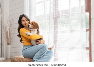 Happy Asian young woman in casual clothes hugging her beagle dog sitting near window in living room at cozy home. Pet and cute animal concept. - Powered by Shutterstock