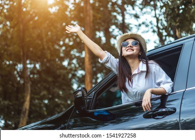 Happy Asian Young Woman Enjoying A Ride In A Car With Hand Greeting. The Concept Of Road Travel And Adventure. 