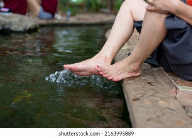 A Happy Asian Young Woman Relaxing In A Hot Spring And Using Her Foot To Bail Out The Water.