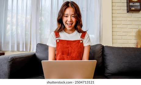 Happy asian young woman sit sofa at home or workplace typing on laptop receive great news celebrating moment of victory, personal achievement, Excited young woman celebrating success with fists raised - Powered by Shutterstock