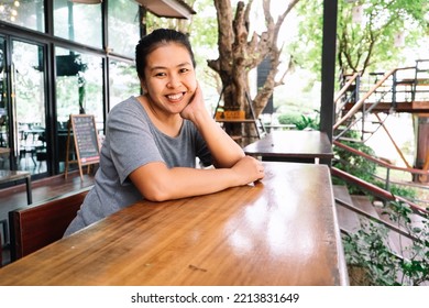 Happy Asian Young Woman Sitting In The Coffee Shop. One Female Only Enjoying At The Cafe In The City. Lady Girl While Relaxing Outside The Restaurant.