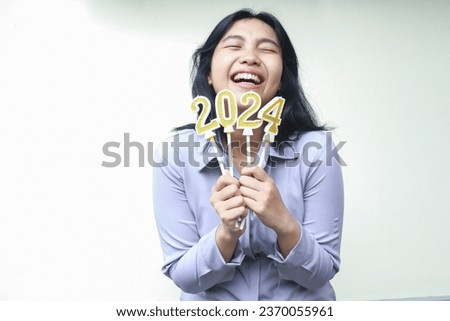 happy asian young woman wear grey formal suit laughing with closed eye and lifting arm hold 2024 figure candle wish for new resolution on new years eve, isolated on white
