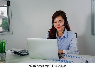 Happy asien junge Geschäftsfrau mit kabellosen Kopfhörern, Blick auf den Bildschirm, winkt hallo. Angenehme attraktive gemischte Rasse weibliche professionelle Durchführung Video-Call mit Klient.