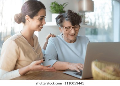 Happy assistant teaching an elderly woman searching the Internet on a laptop