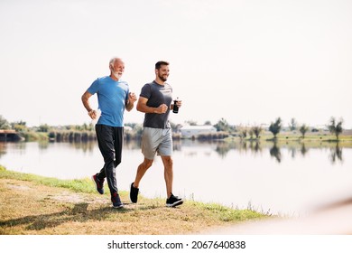 Happy athlete and his senior father jogging by the lake in nature. Copy space. - Powered by Shutterstock