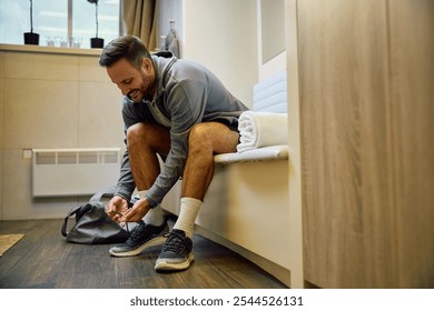 Happy athlete tying shoelace at gym's locker room. Copy space. - Powered by Shutterstock