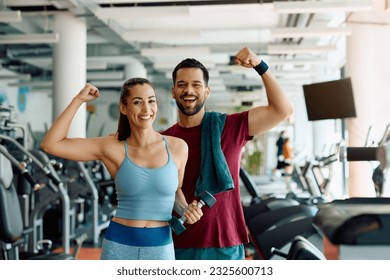 Happy athletic couple flexing their muscles after working out in a gym and looking at camera.
