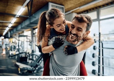 Happy athletic couple having fun while piggybacking in health club.