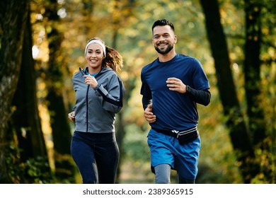 Happy athletic couple jogging during autumn day in the park.