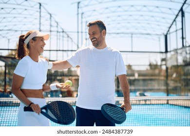 Happy athletic couple laughing while playing paddle tennis on outdoor court. Copy space. - Powered by Shutterstock