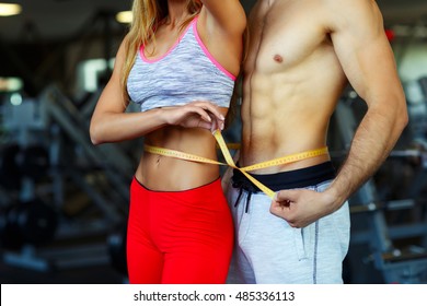 Happy athletic couple - man and woman with measuring tape in gym