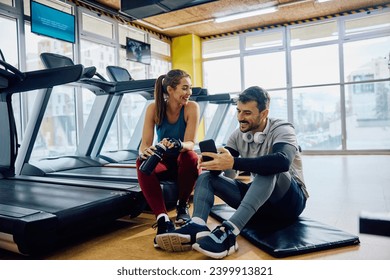 Happy athletic couple using cell phone while taking a break from exercising in health club. - Powered by Shutterstock